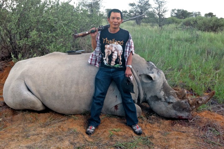 A man standing with a gun in front of a dead rhino
